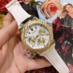 Guess Zena W1094L1 women's multi-function watch, with a gold-tone and stainless steel case, white dial, and a white silicone rubber strap.